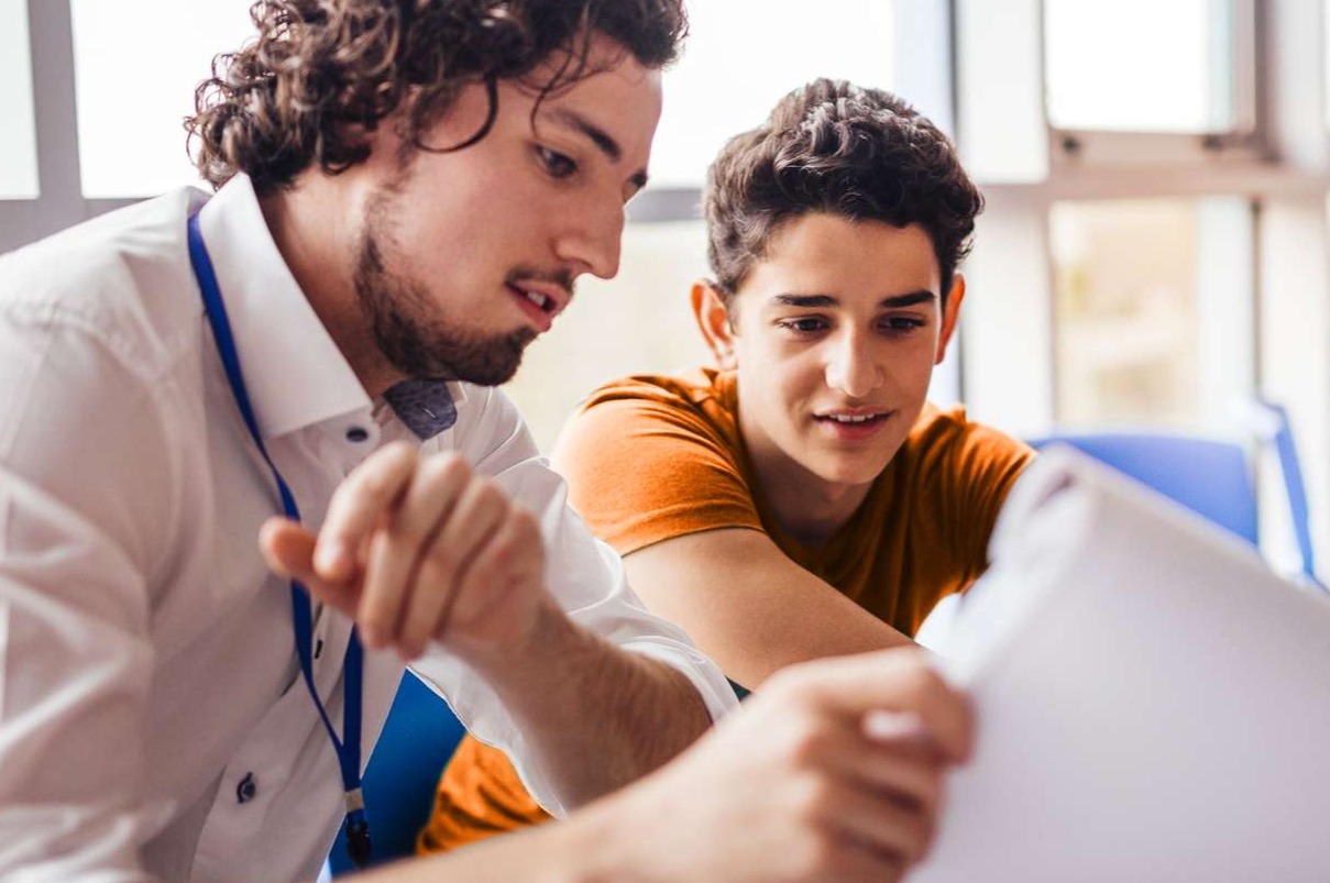 adult male tutor looking at paper with male student